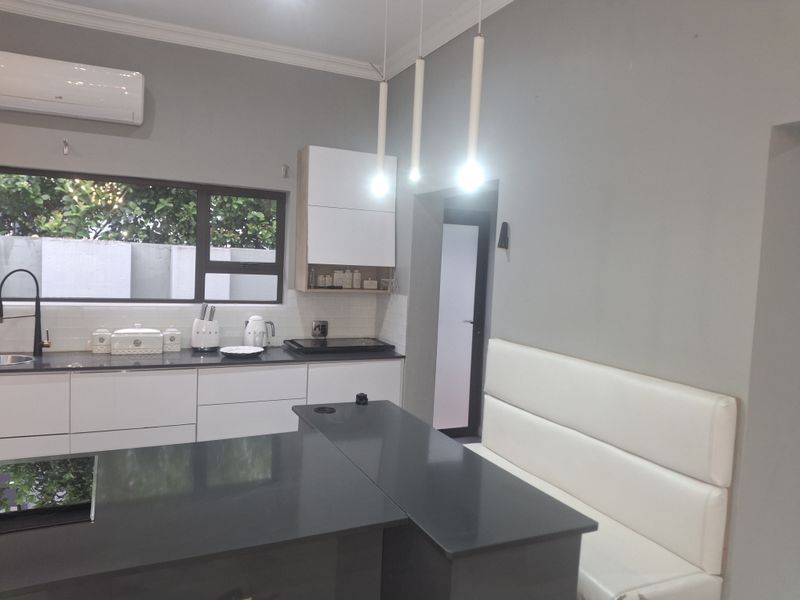 Modern kitchen featuring sleek white cabinetry, dark stone countertops, integrated bench seating, and contemporary pendant lighting with a split-system air conditioner.