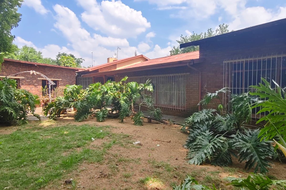Rear view of a brick house featuring a garden area with established plants and security bars on the windows.