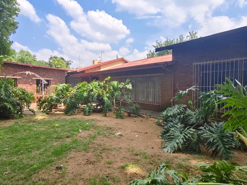 Rear view of a brick house featuring a garden area with established plants and security bars on the windows.