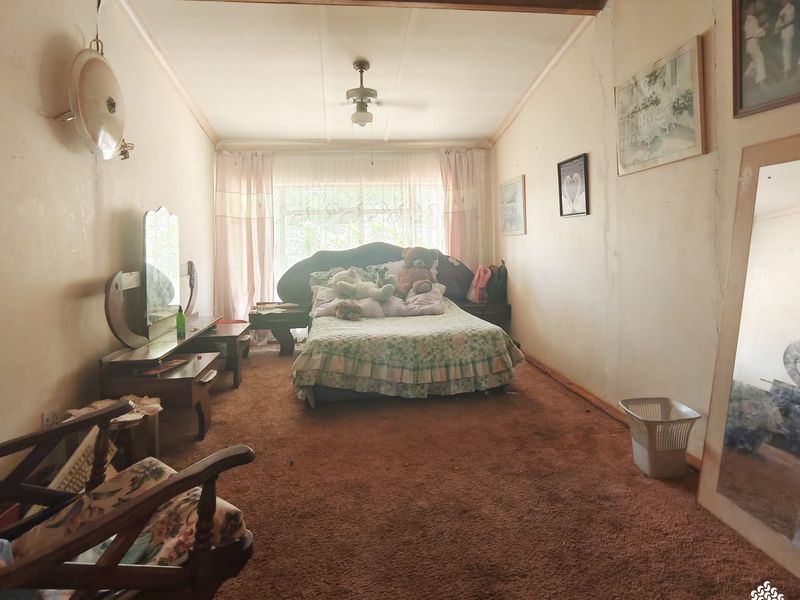 A bedroom featuring carpet flooring, a ceiling fan, and a large window. The room shows signs of wear and requires cosmetic updates.