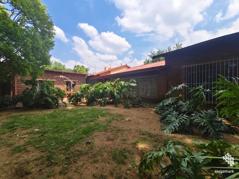 A view of the rear exterior of the house featuring face brick walls, metal security bars on windows, and a garden area.
