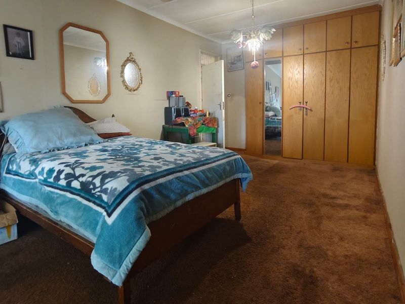 Spacious bedroom featuring built-in wooden cupboards and carpeted flooring, showing signs of ceiling water damage and general wear.
