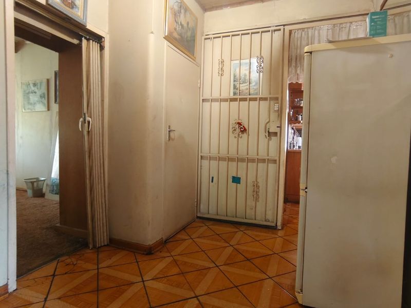 A functional hallway featuring patterned floor tiles, a wooden ceiling, and a security gate, showing signs of age and wear throughout.