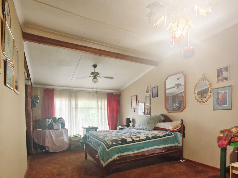 A bedroom featuring carpet flooring, a ceiling fan, and a central chandelier, showing signs of wear and a visible ceiling stain.