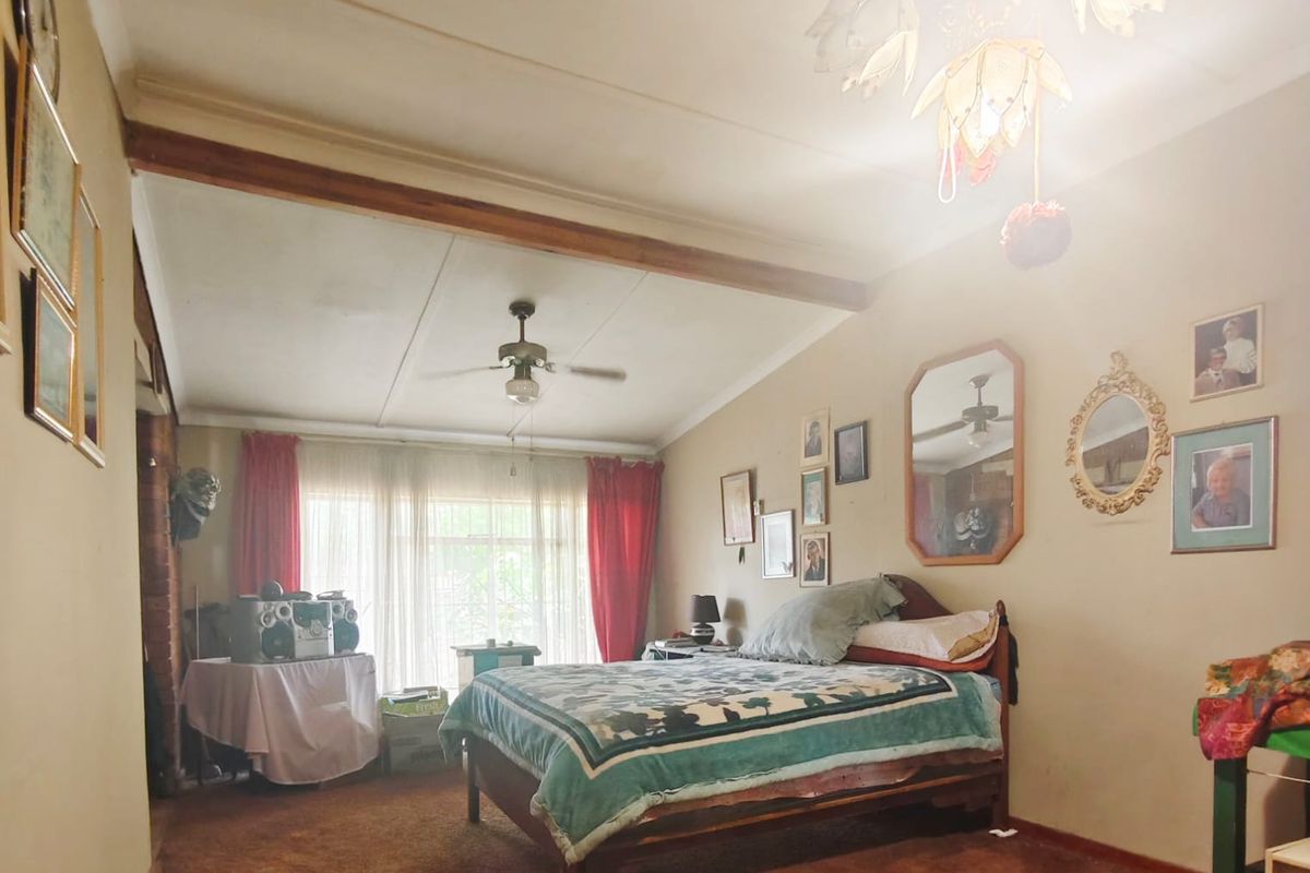 A bedroom featuring carpet flooring, a ceiling fan, and a central chandelier, showing signs of wear and a visible ceiling stain.