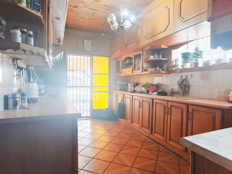 A dated kitchen featuring extensive wooden cabinetry, timber ceiling, and tiled flooring, offering a functional layout with potential for modern renovation.