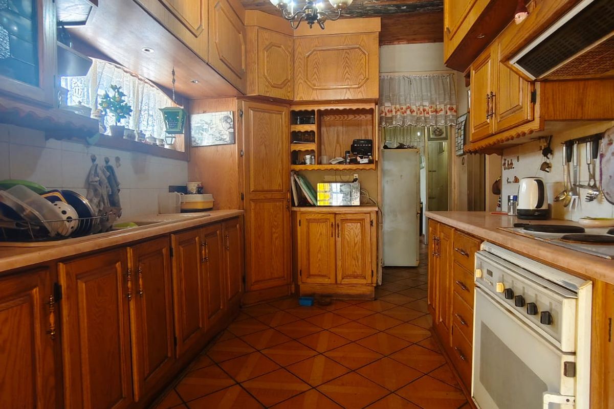 A traditional kitchen featuring extensive wooden cabinetry, a timber-clad ceiling, and tiled flooring, offering a classic layout with integrated cooking appliances.