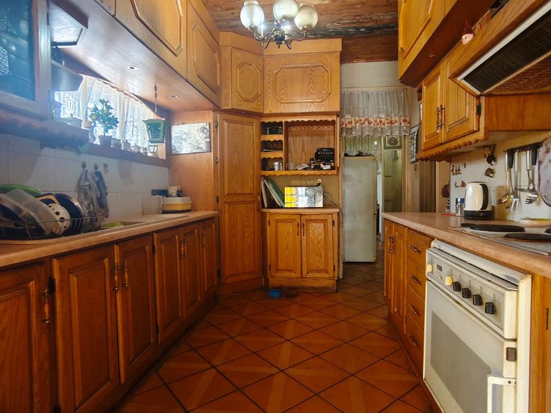 A traditional kitchen featuring extensive wooden cabinetry, a timber-clad ceiling, and tiled flooring, offering a classic layout with integrated cooking appliances.