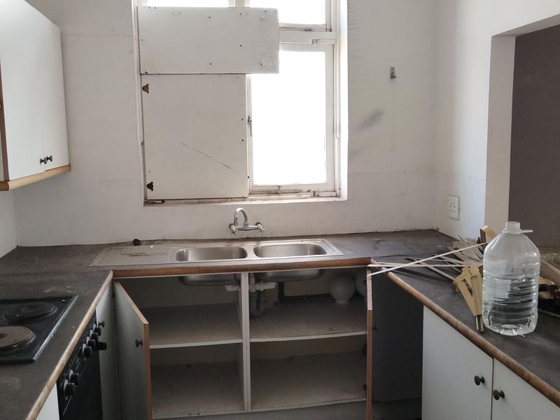 A dated kitchen featuring a double bowl sink, built-in oven and hob, and base cabinetry, requiring significant renovation and repair to the window and finishes.