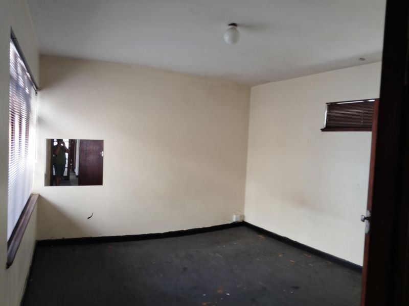An empty bedroom featuring venetian blinds, a wall-mounted mirror, and dark flooring, offering a blank canvas for renovation or interior design updates.