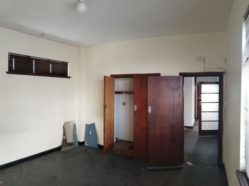 An empty bedroom featuring a built-in wooden wardrobe, venetian blinds, and dark flooring, requiring cosmetic updates to restore its appeal.