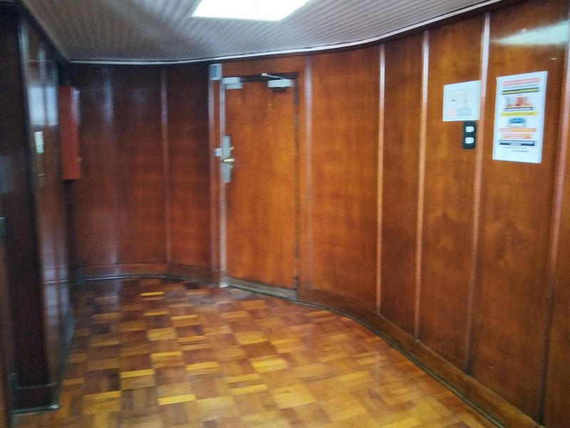 A spacious hallway featuring classic wood paneling and parquet flooring, illuminated by a recessed ceiling light.