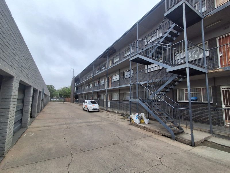 Exterior view of a multi-story apartment block featuring a concrete driveway, external steel staircases, and a row of garages.