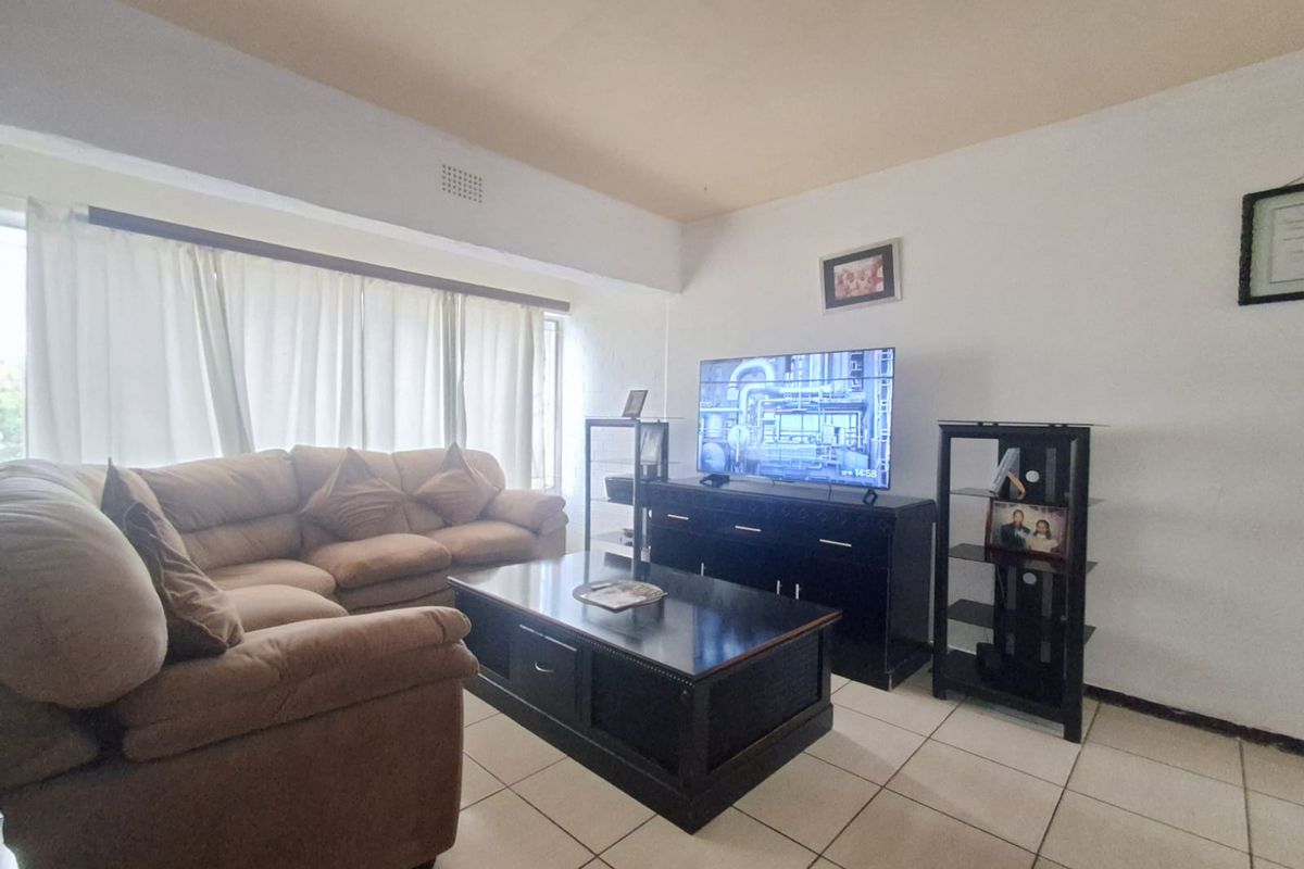A living room featuring tiled flooring and large windows with curtain rails, providing a functional and well-lit space.