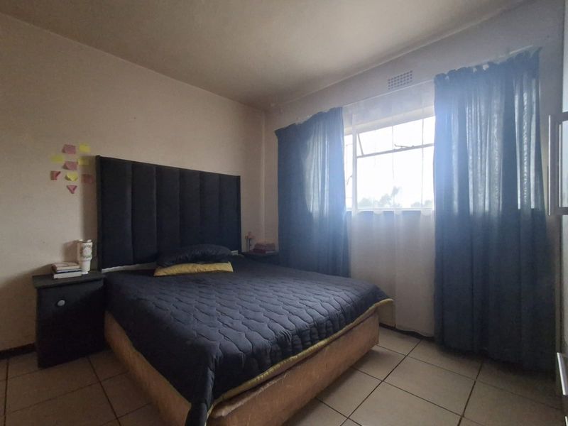 A standard bedroom featuring tiled flooring and a window with security bars, offering a functional space with potential for cosmetic updates.