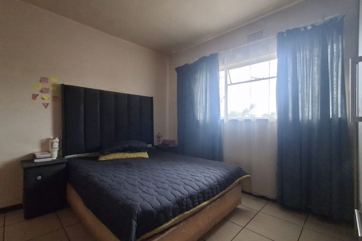 A standard bedroom featuring tiled flooring and a window with security bars, offering a functional space with potential for cosmetic updates.