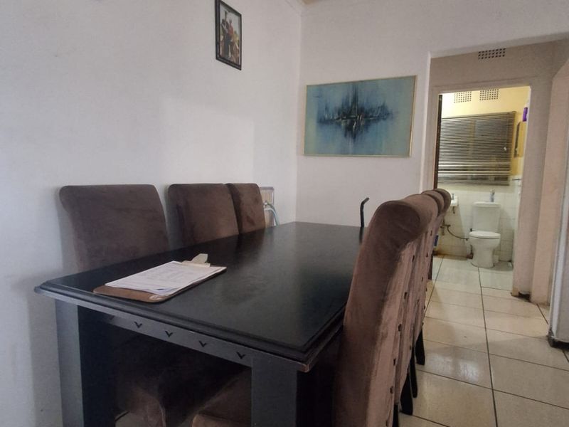 A dining area featuring tiled flooring and coved ceilings, with a clear view through to the adjacent bathroom.