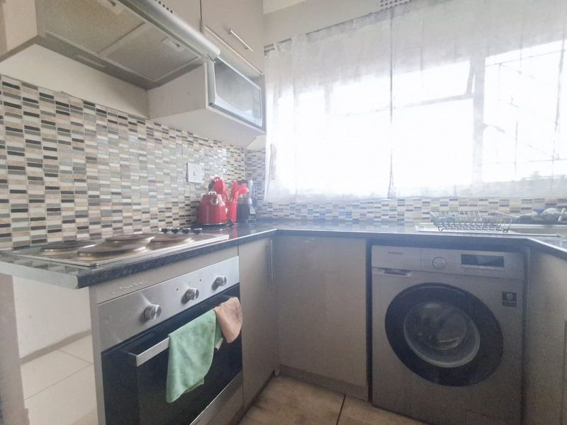 A functional kitchen featuring built-in cabinetry, a mosaic tile backsplash, an electric hob with oven, and space for an integrated washing machine.