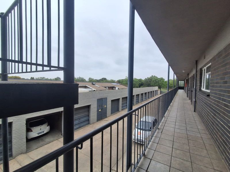 An elevated exterior walkway or balcony featuring metal railings and tiled flooring, overlooking a row of garage units.