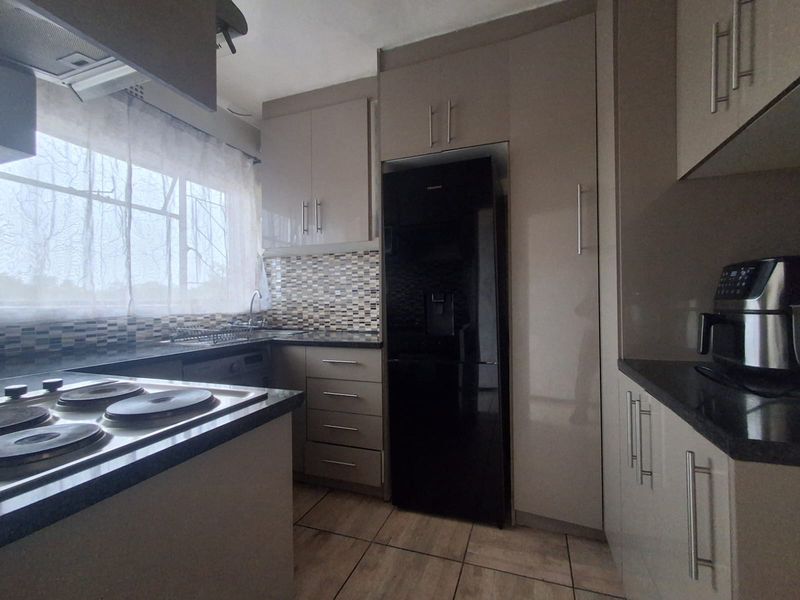 Modern kitchen featuring sleek built-in cabinetry, granite countertops, a mosaic tile backsplash, and integrated electric hob with extractor fan.