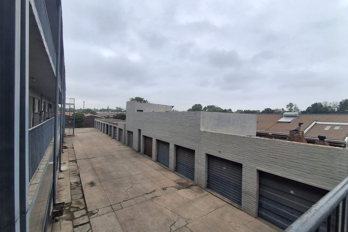 View of the rear exterior area featuring a row of garages with a concrete driveway and metal balcony railings.