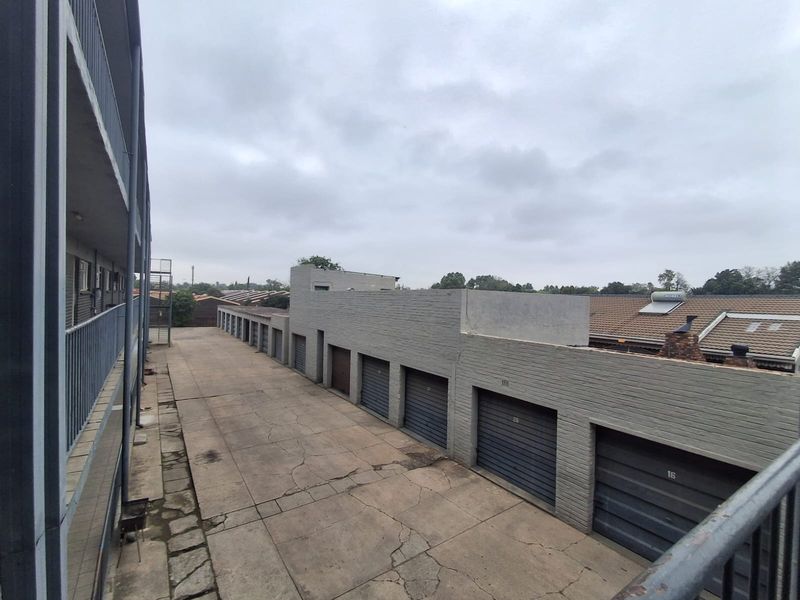 View of the rear exterior area featuring a row of garages with a concrete driveway and metal balcony railings.