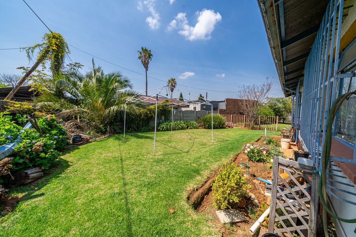 A rear garden area featuring a lawn, perimeter wall, and security bars on the building exterior.