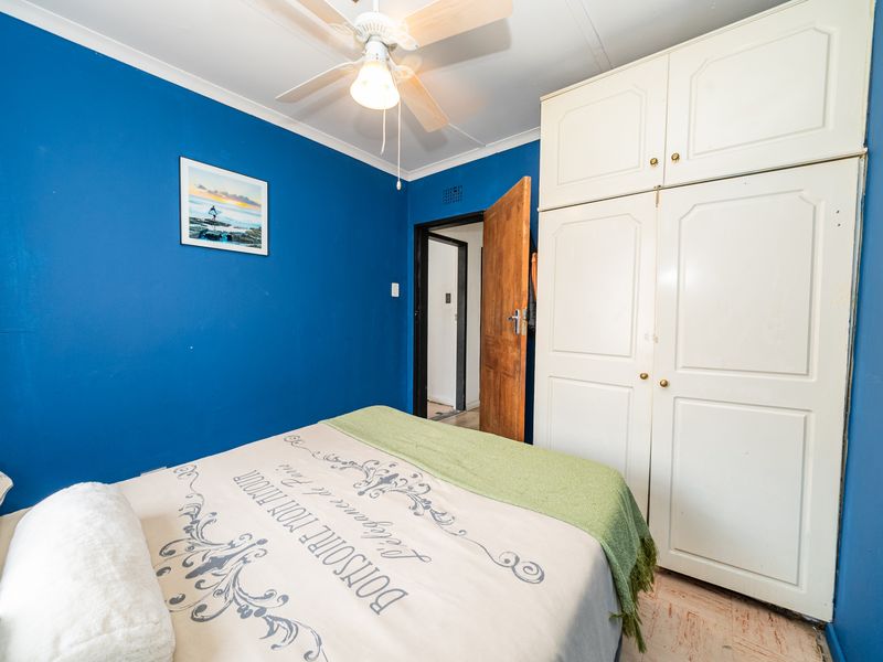 A bedroom featuring a built-in wardrobe, ceiling fan, and blue accent wall, providing a functional space with potential for cosmetic updates.