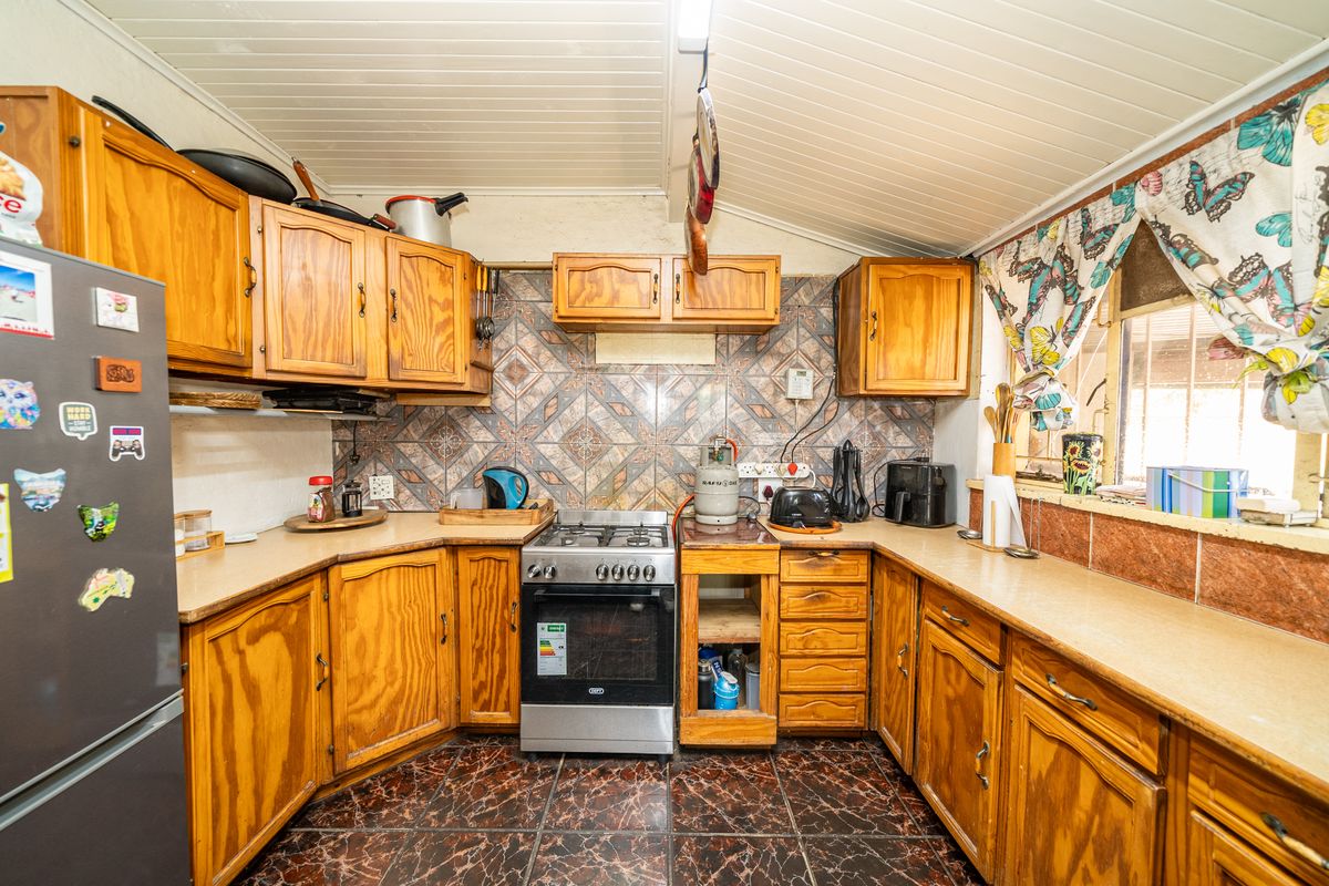 A dated kitchen featuring wooden cabinetry, laminate countertops, a gas stove, and patterned tile backsplash with tiled flooring.