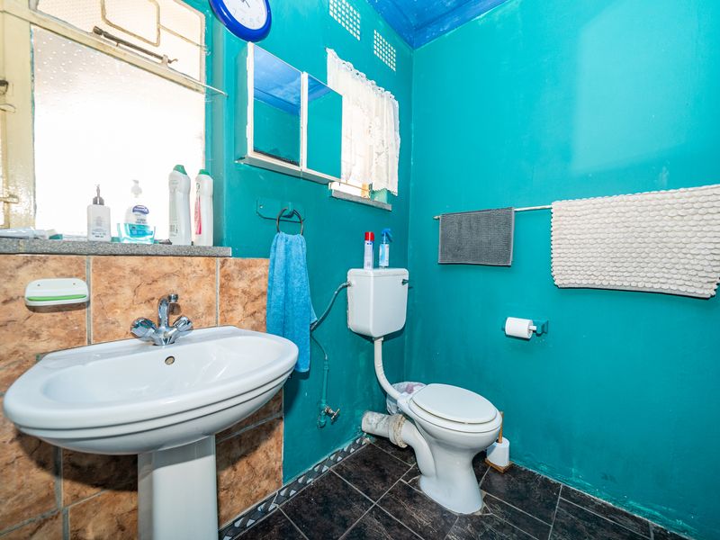 A functional bathroom featuring a pedestal basin, toilet, and tiled splashback, currently finished with bold wall paint and requiring some cosmetic updates.
