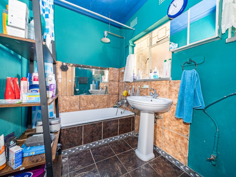 A functional bathroom featuring a pedestal washbasin, bathtub with shower head, and tiled finishes, offering potential for modernization and aesthetic updates.