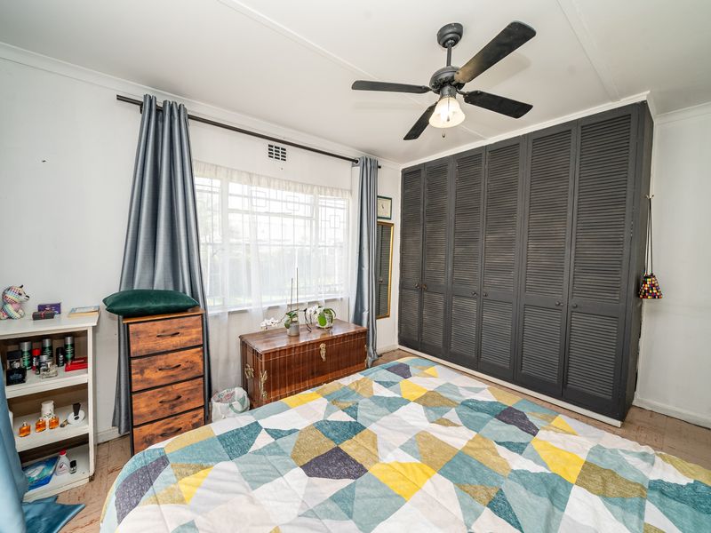 A bedroom featuring built-in dark louvered cupboards, a ceiling fan, and a window with natural light.