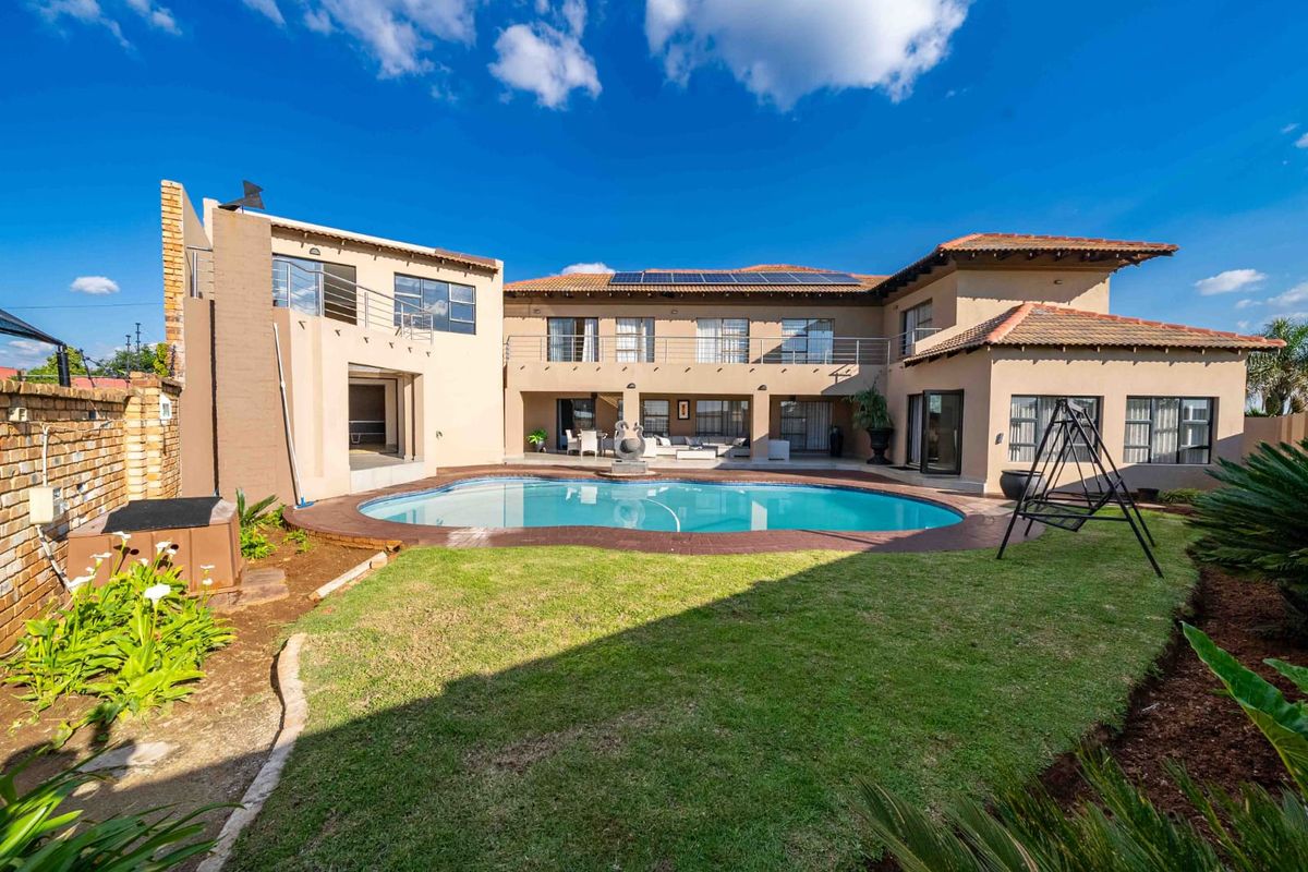 Spacious rear exterior view featuring a large swimming pool, landscaped garden, paved patio, and a multi-level house with solar panels and balcony access.