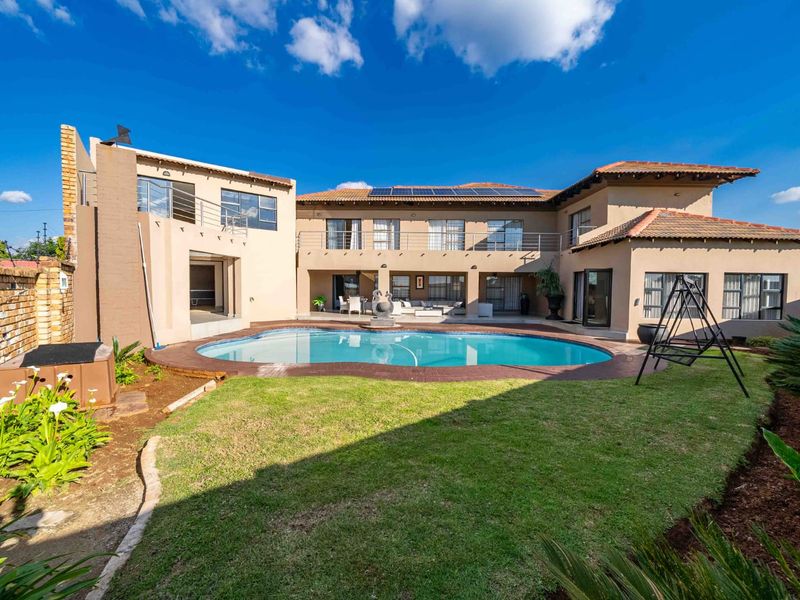 Spacious rear exterior view featuring a large swimming pool, landscaped garden, paved patio, and a multi-level house with solar panels and balcony access.
