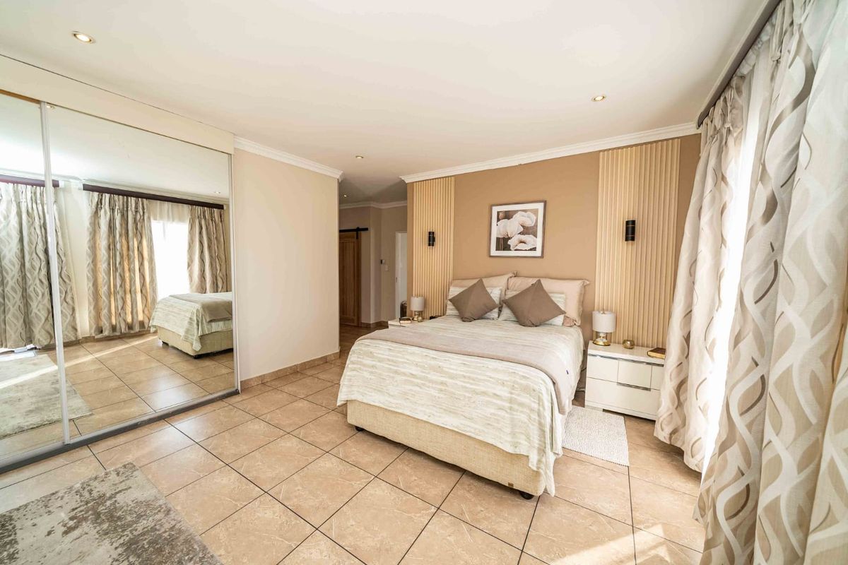 Spacious bedroom featuring tiled flooring, mirrored sliding wardrobes, and decorative wall paneling with integrated lighting fixtures.