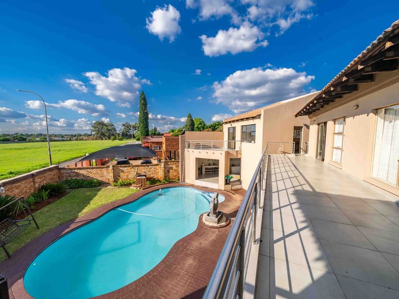 Spacious rear exterior featuring a swimming pool, paved surround, and an elevated tiled balcony with stainless steel balustrades overlooking the garden.
