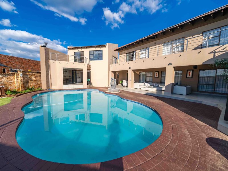 Spacious rear exterior featuring a large swimming pool, brick paved surround, covered patio area, and a two-story residence with balcony access.