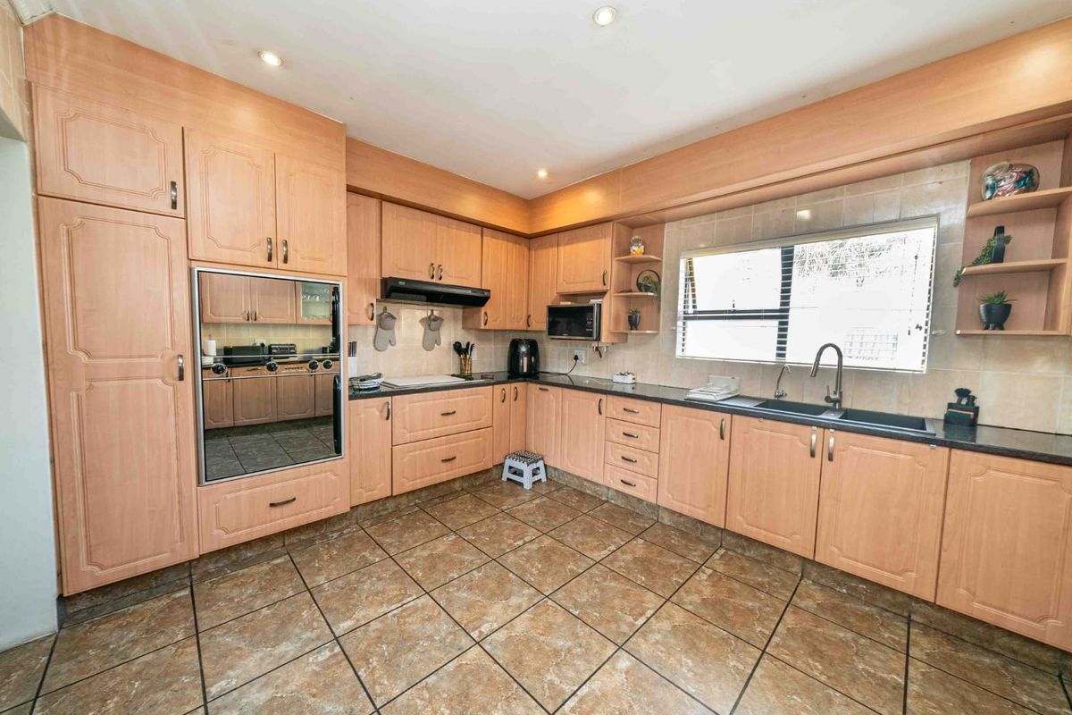 A functional kitchen featuring light wood-finish cabinetry, dark countertops, tiled flooring, and integrated appliances, offering a classic layout with ample storage space.