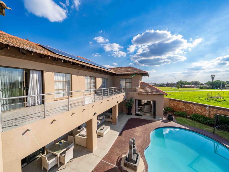 Spacious rear exterior featuring a swimming pool, covered patio, and an upper-level balcony with stainless steel railings overlooking the garden and surrounding landscape.
