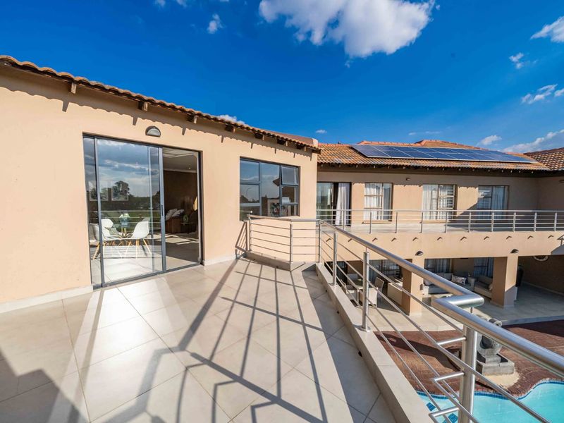 Spacious upper-level balcony featuring tiled flooring, stainless steel balustrades, and direct access to the interior, overlooking the swimming pool and rear garden area.