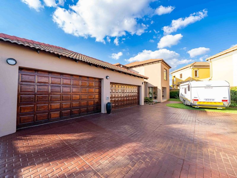 Front view of the property featuring a spacious paved driveway and a double garage with wooden doors.