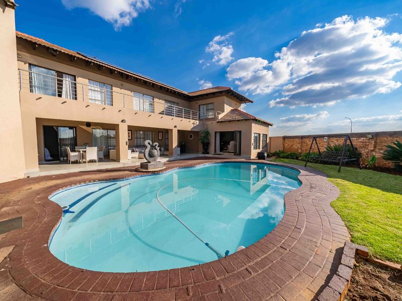Spacious rear garden featuring a swimming pool with brick coping, a covered patio area, and an upper-level balcony with stainless steel railings.