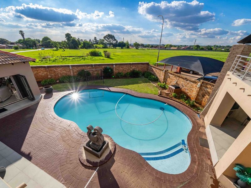 An elevated view of a backyard featuring a swimming pool with paved surround, brick boundary walls, and a shade sail structure.