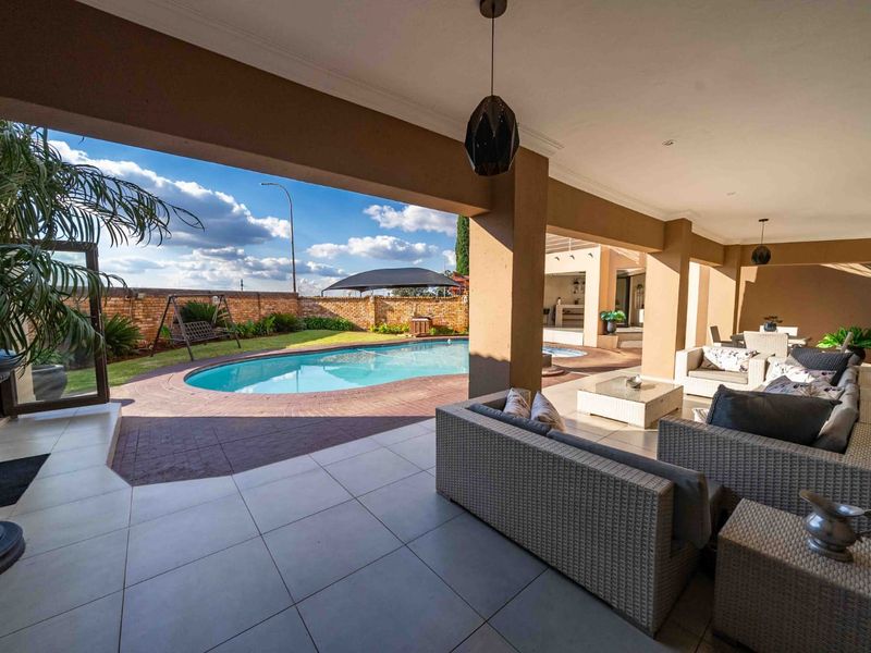 Spacious covered patio overlooking a private swimming pool and landscaped garden, featuring tiled flooring and integrated lighting, perfect for outdoor entertaining.