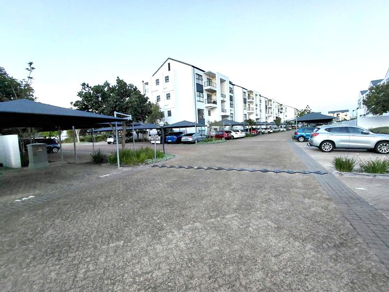 Exterior view of the apartment complex featuring paved parking areas with covered carports and a multi-story residential building.