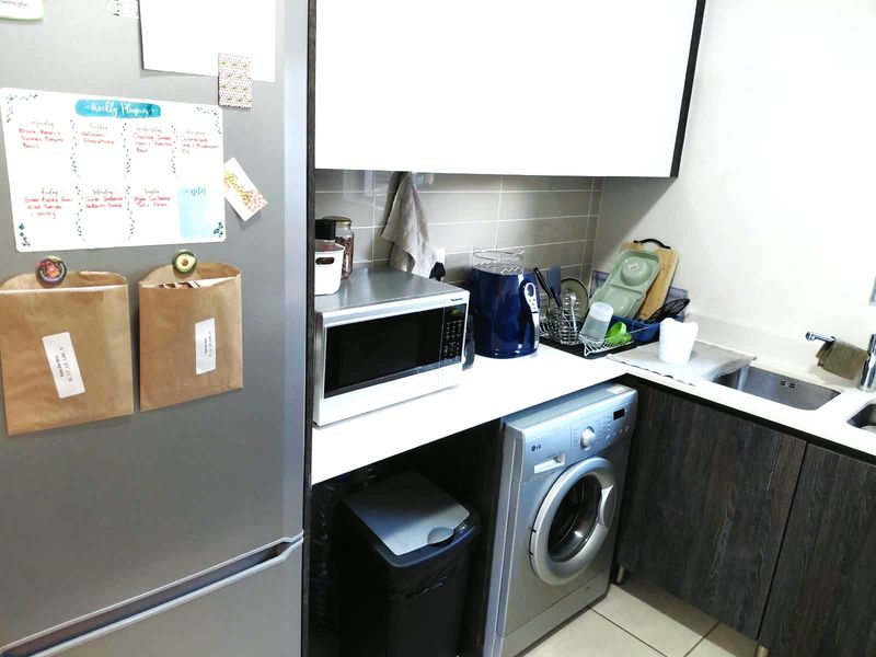 Compact laundry area featuring built-in cabinetry, a stainless steel sink, tiled backsplash, and an integrated washing machine.