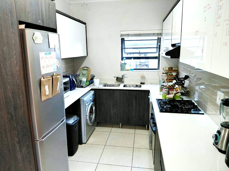 Compact kitchen featuring modern two-tone cabinetry, gas hob, extractor fan, double sink, and tiled flooring with a functional layout.