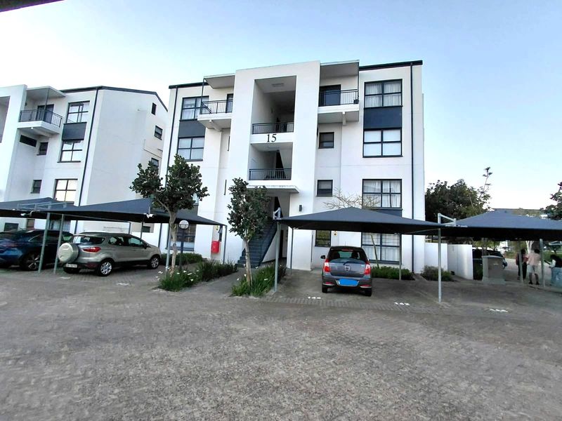 Front elevation of a modern apartment complex featuring covered parking bays, balconies, and a paved driveway area.