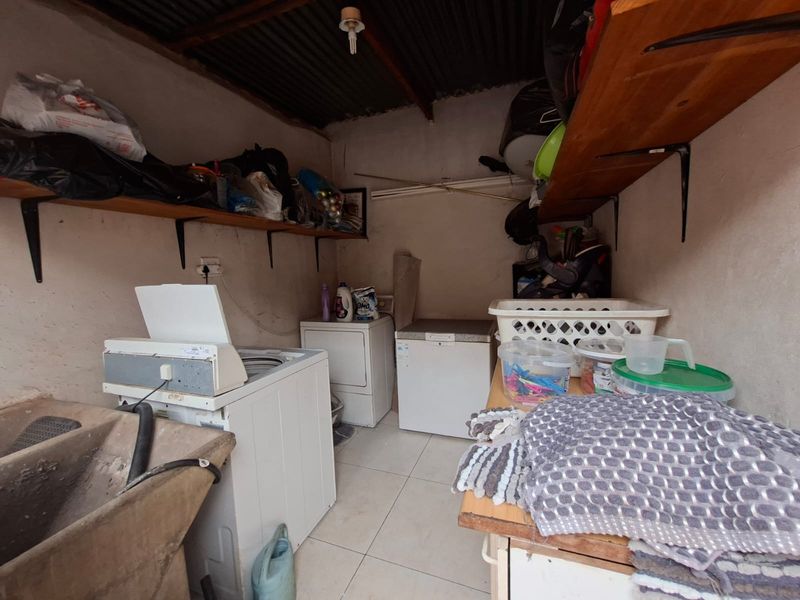 A functional laundry area featuring a concrete sink, tiled floors, and wall-mounted storage shelving with an exposed corrugated metal ceiling.