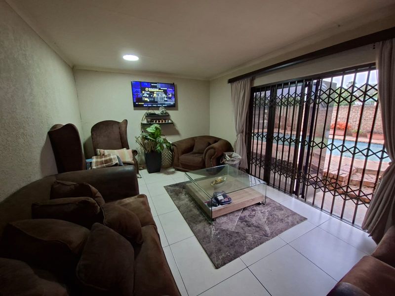 A comfortable living room featuring tiled flooring and large sliding glass doors with security gates, providing direct access to the outdoor pool area.